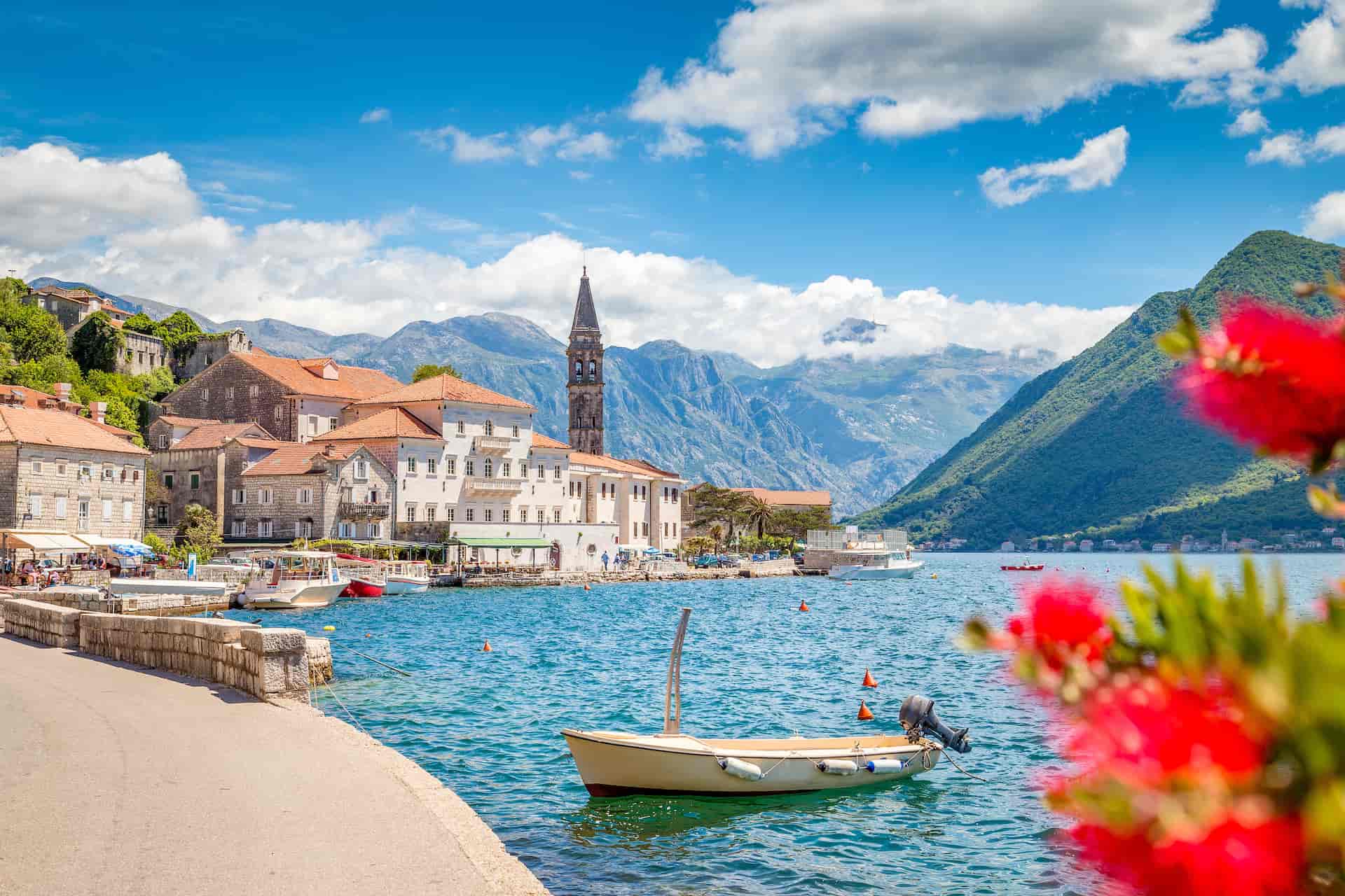 Small boat floating on blue water near coastal town with mountains in Montenegro.