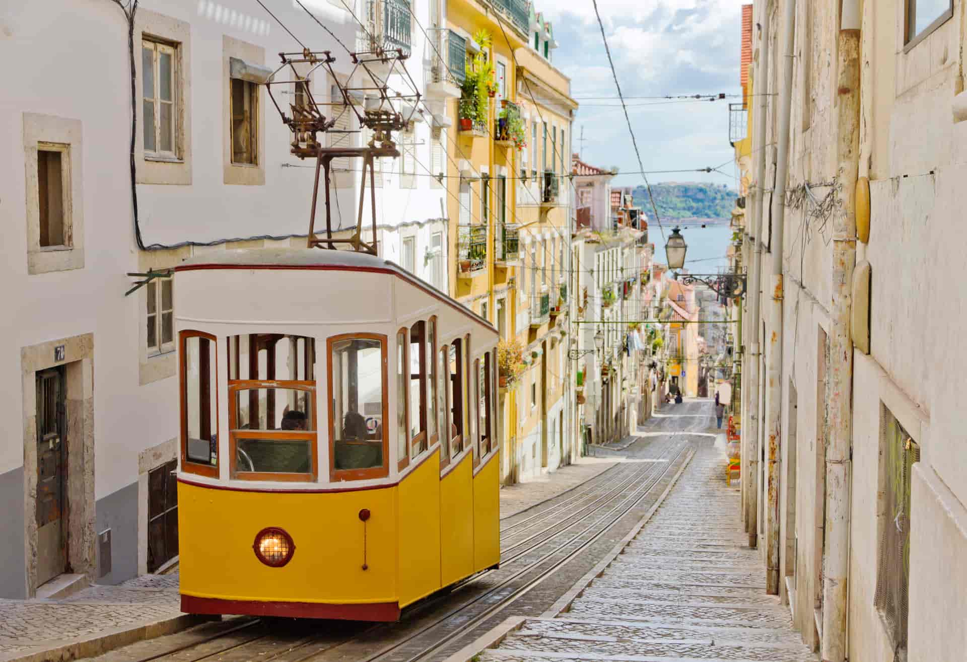 Yellow funicular tram ascending steep cobblestone street between historic buildings in Portugal.