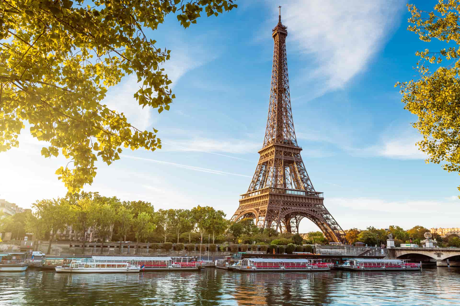 Eiffel Tower over Seine River with tour boats docked, framed by yellowing autumn leaves in Paris.