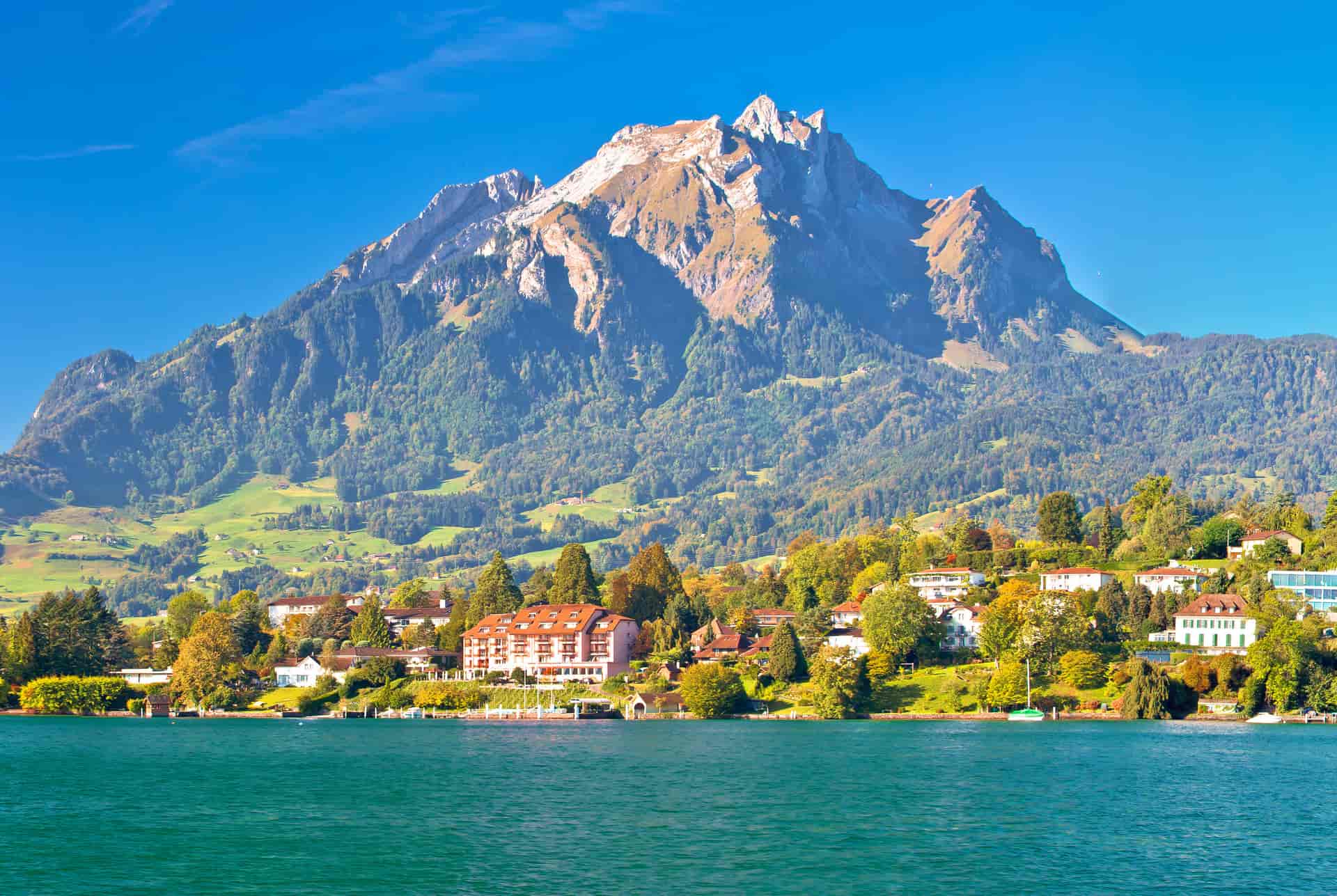 Alpine lake with turquoise water, town, and large mountain under clear blue sky in Switzerland.