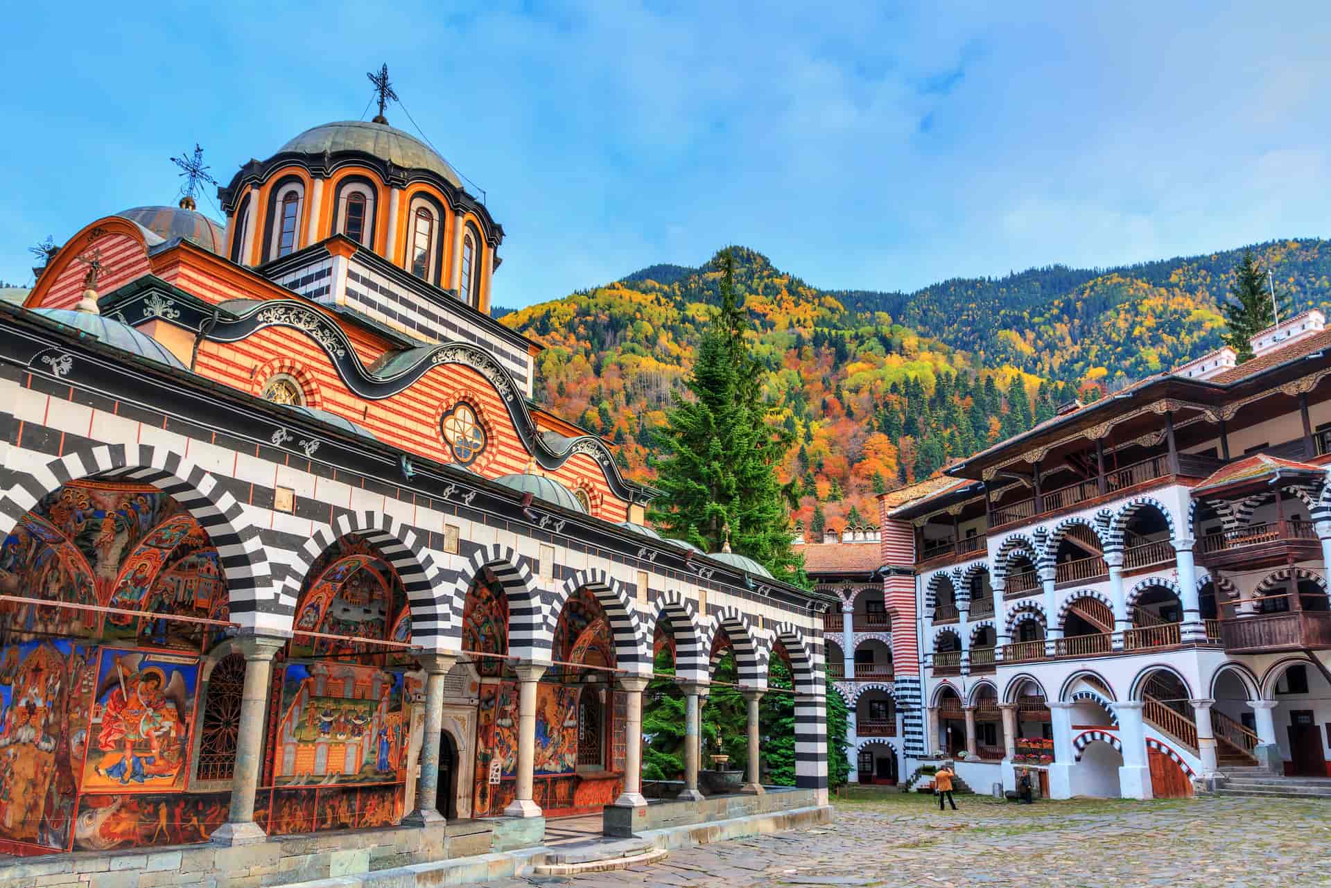 Rila Monastery with colorful frescoes and autumn foliage on mountain backdrop, Bulgaria.