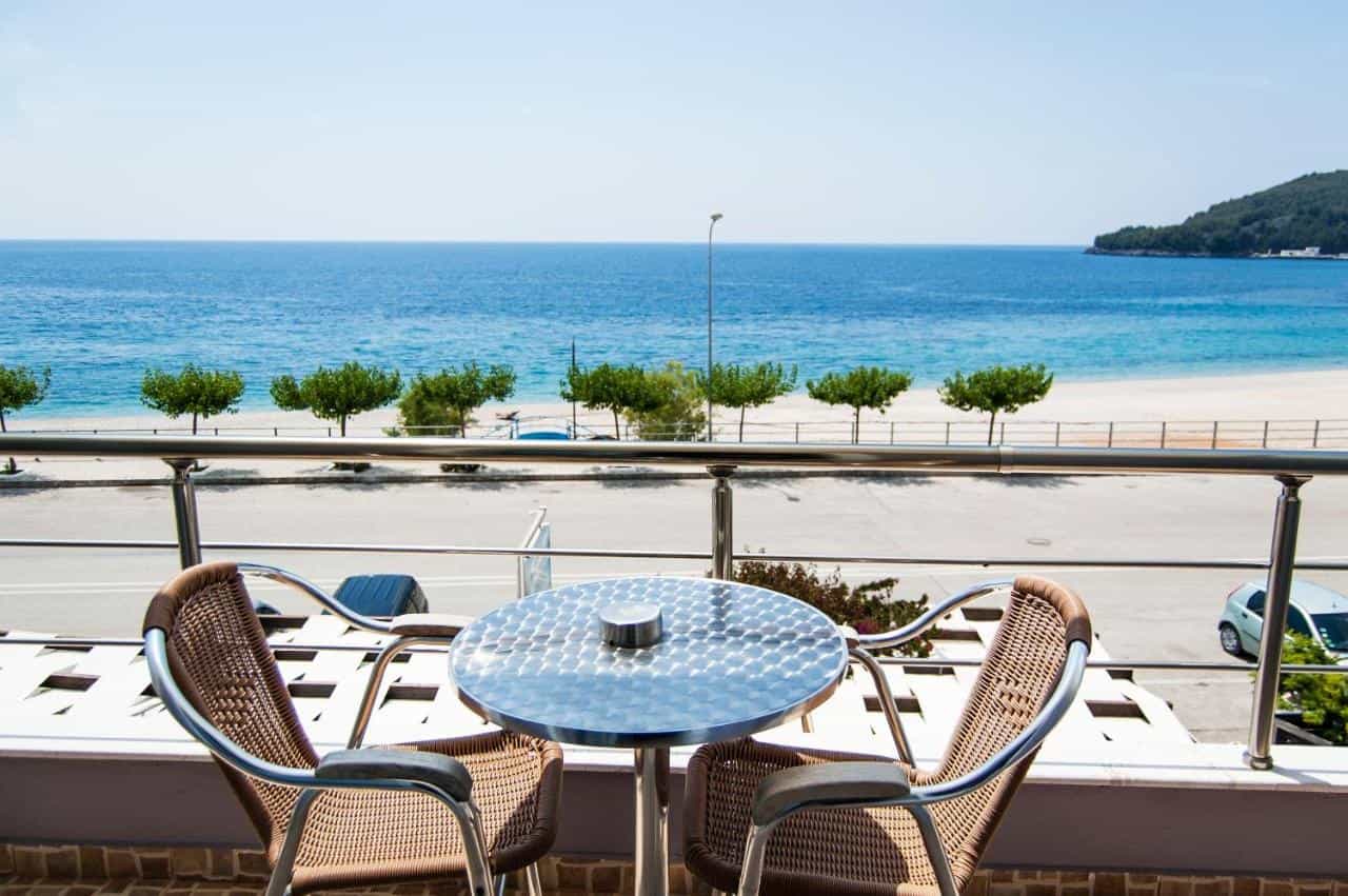 Balcony with wicker chairs and metal table overlooking beach, road, and blue sea in Himare.