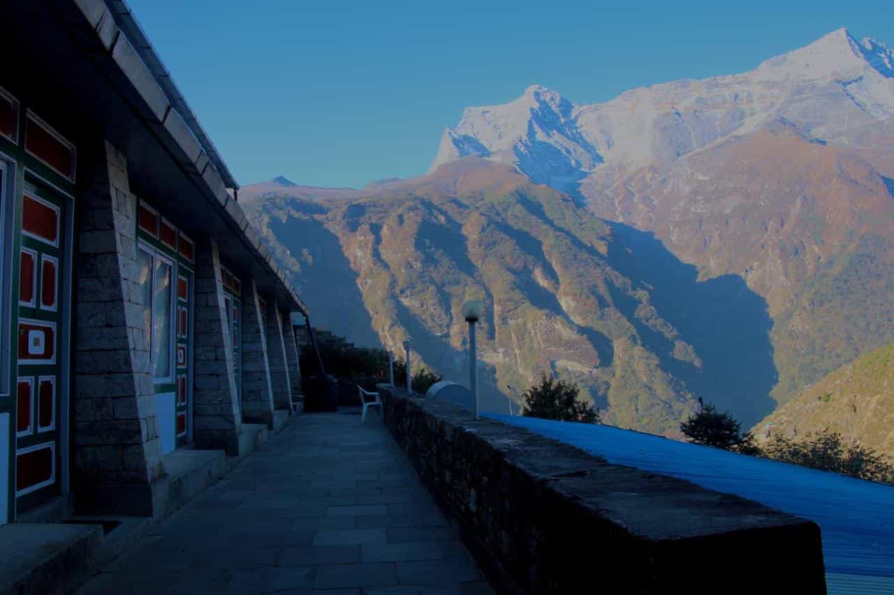 Lodge walkway with stone pillars overlooking massive, sunlit Himalayan mountains near Namche Bazaar.