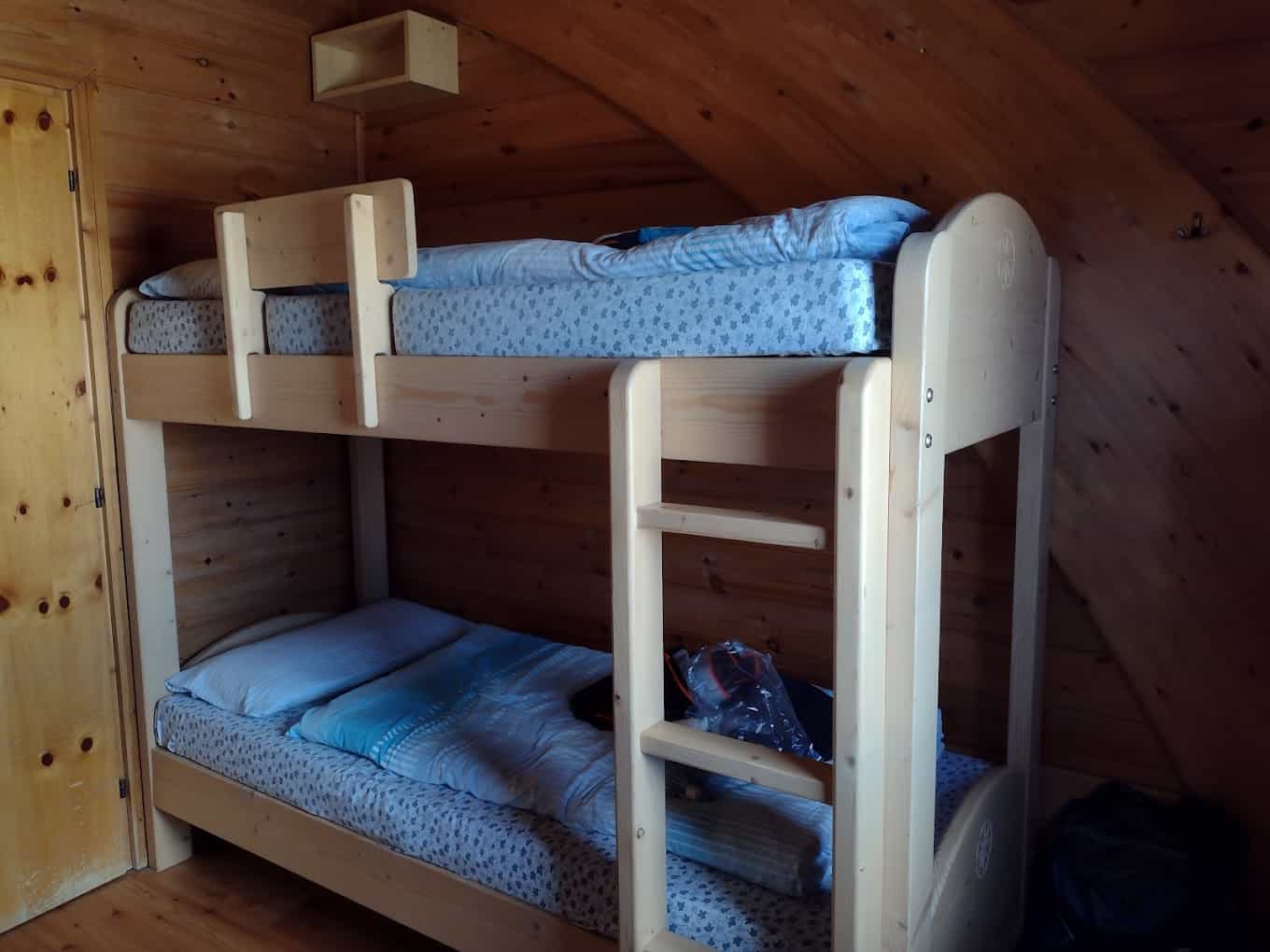 Wooden bunk beds with blue bedding inside a room with angled wood-paneled walls.