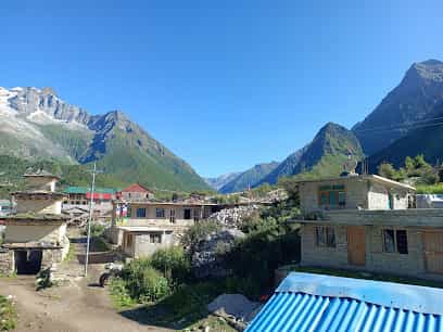 Village buildings nestled in a valley surrounded by steep, green and snow-capped mountains under a clear blue sky.