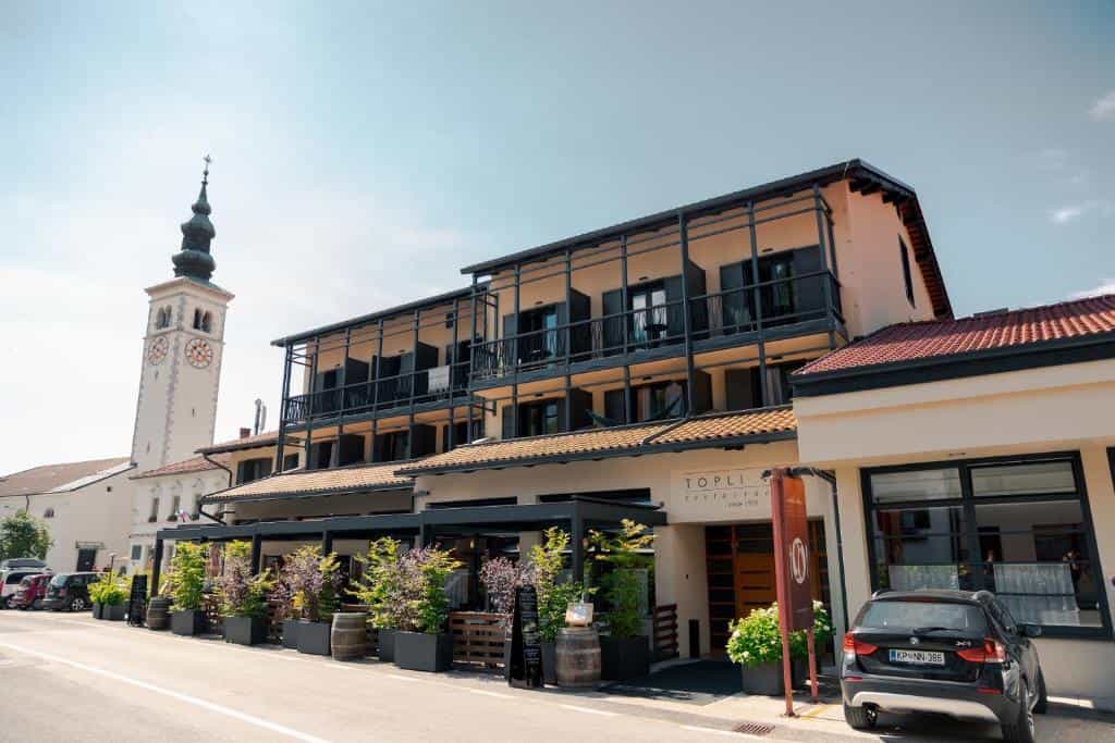 Hotel Topli restaurant next to a tall white clock tower on a sunny day.