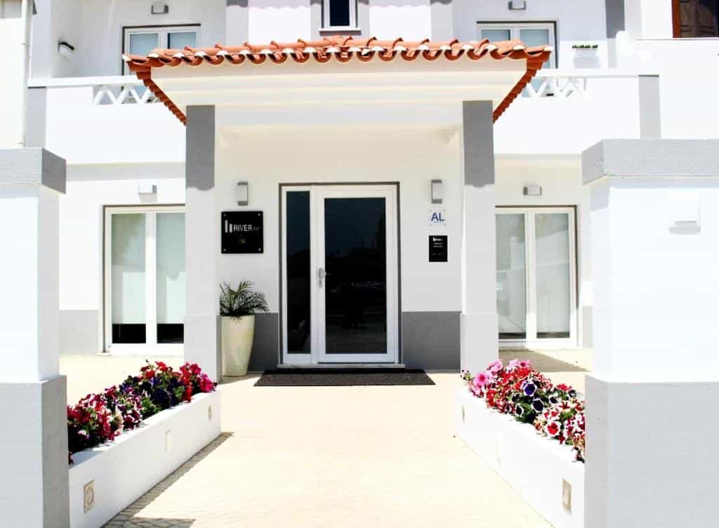Entrance to River Inn Duna Parque Resorts hotel with white facade and flower boxes.