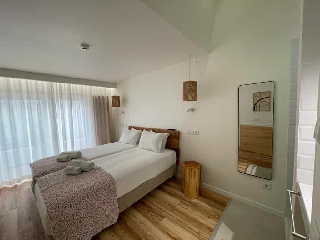 Twin beds with white linens, patterned throw, and wooden accents in a bright hotel room.