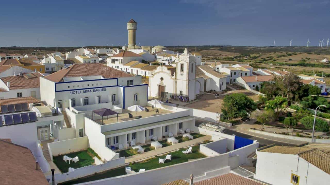 Hotel Mira Sagres in white village with church, water tower, and wind turbines on horizon.