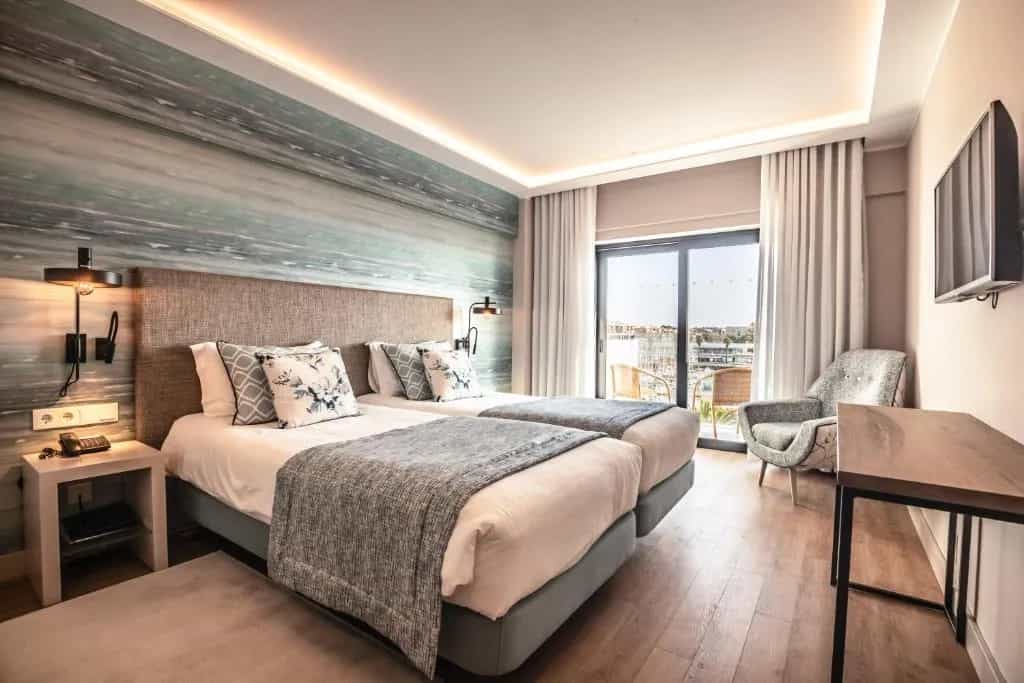 Twin hotel room with sea-themed mural, wood floors, and balcony view of marina.
