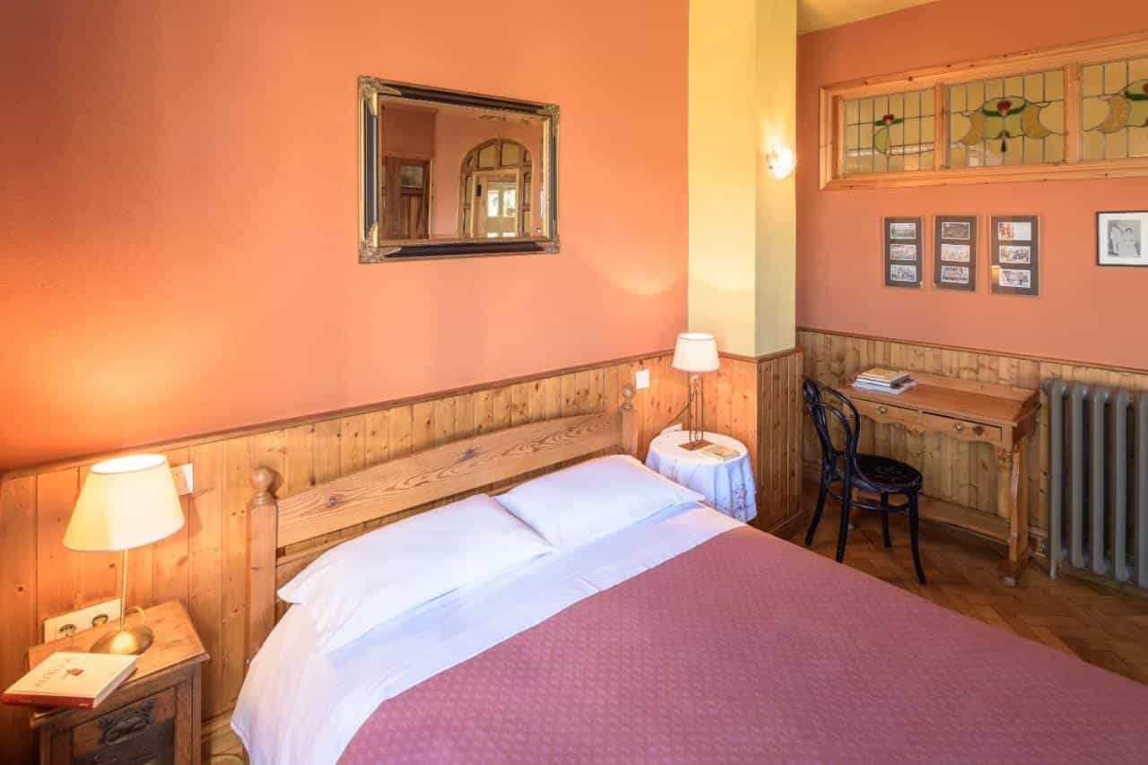Cozy inn room with wooden paneling, pink bedding, framed mirror, and stained glass window.