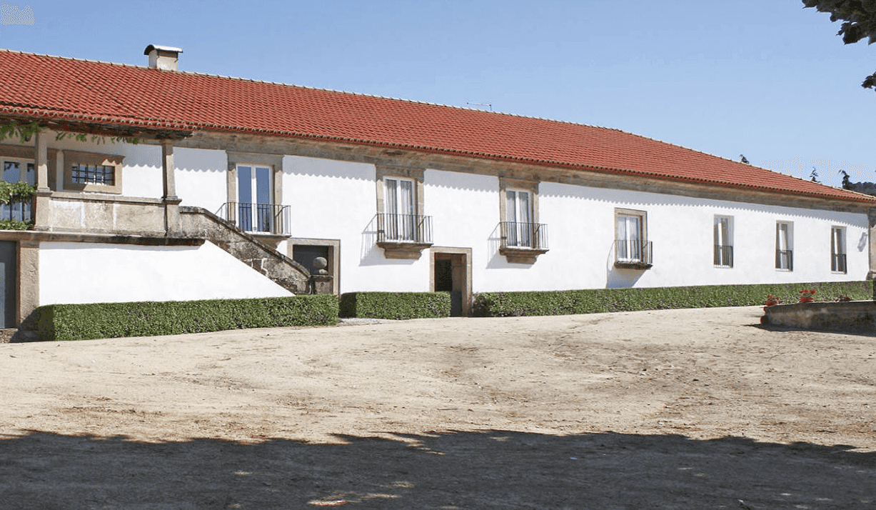 White stucco building with red tile roof, stone trim, and small Juliet balconies under clear blue sky.