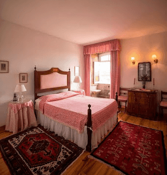 Bedroom with wooden bed, pink bedding, and two red patterned area rugs on a wooden floor.