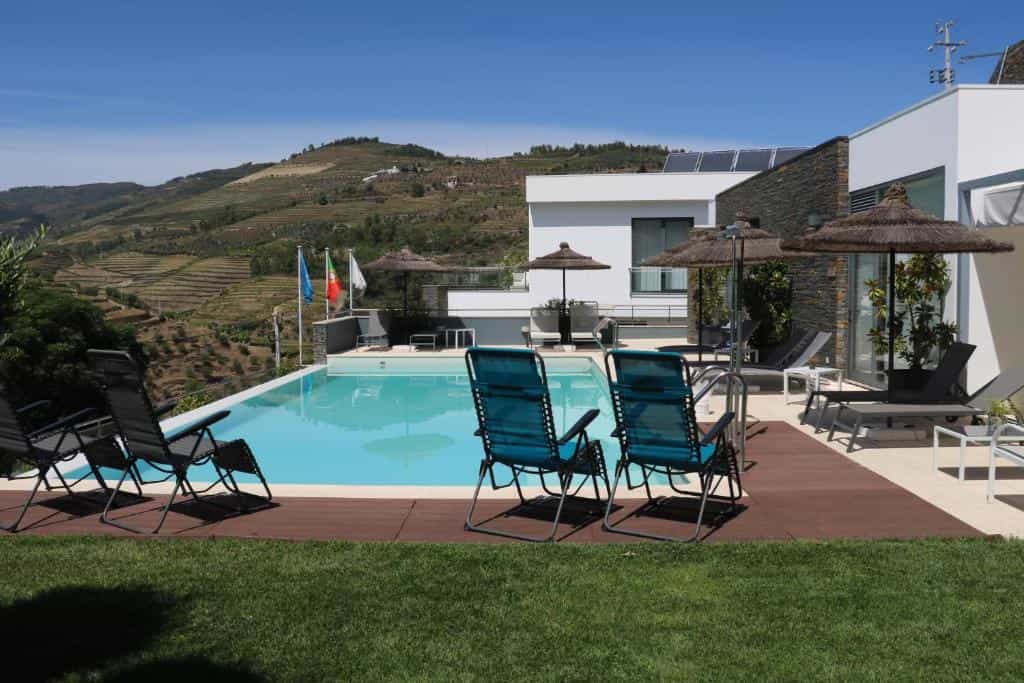 Infinity pool with lounge chairs overlooking terraced hillsides under a clear blue sky.