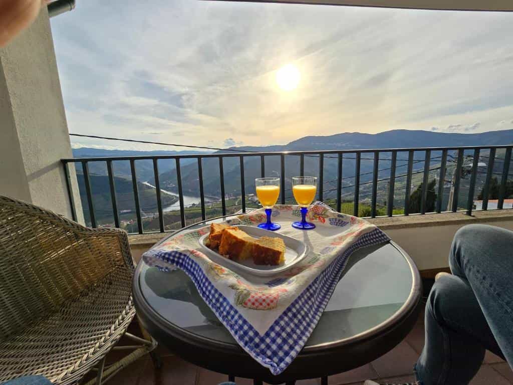 Breakfast with juice and cake on balcony overlooking sunlit river valley and mountains