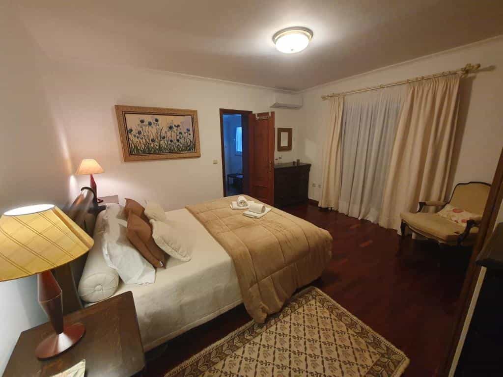 Bedroom with large bed, bedside lamps, dark wood floor, and floral artwork.