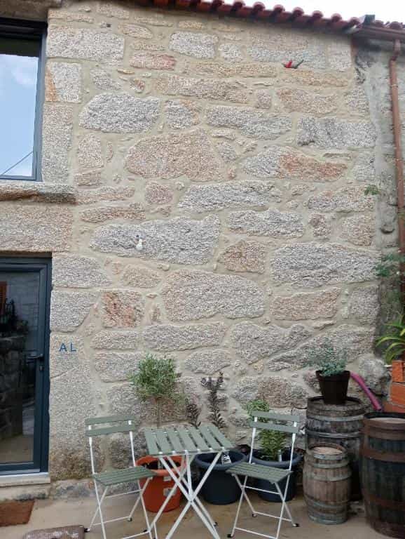 Stone wall exterior with small outdoor seating area, potted plants, and wooden barrels.