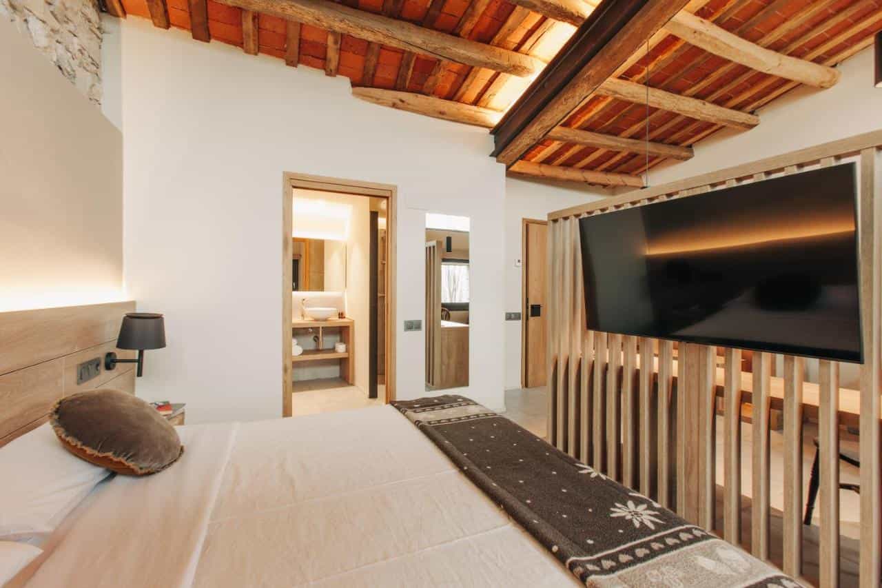 Boutique hotel room with exposed terracotta tile ceiling, wooden accents, and view into bathroom.