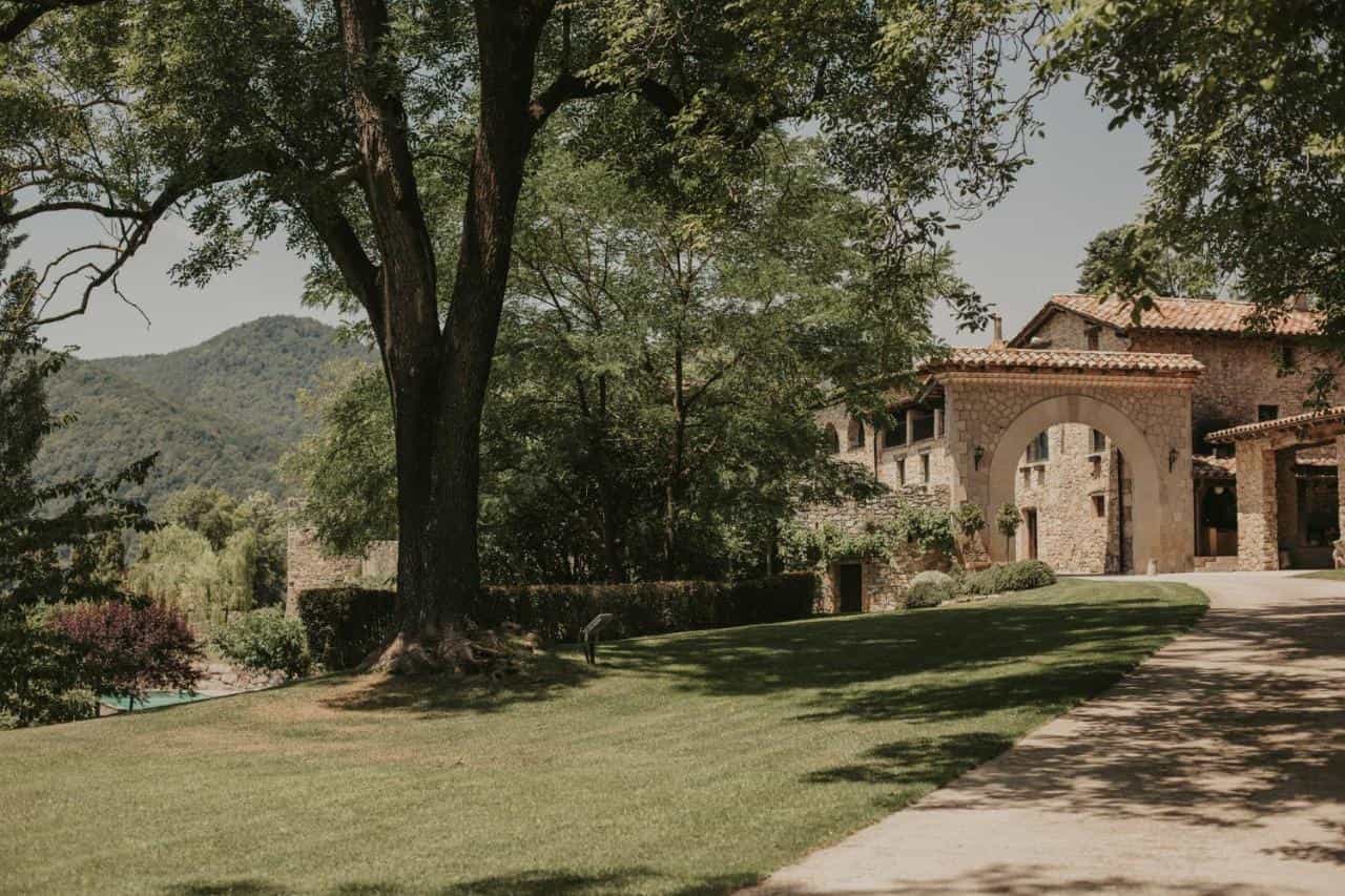 Stone Hotel El Mariner entrance with large tree and green mountains in background
