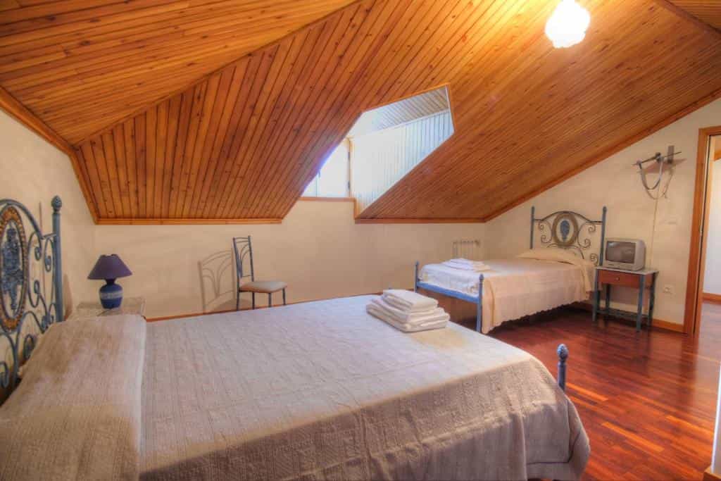 Guest house attic bedroom with wood ceiling, two beds, and hardwood floor in Casa do Destro.