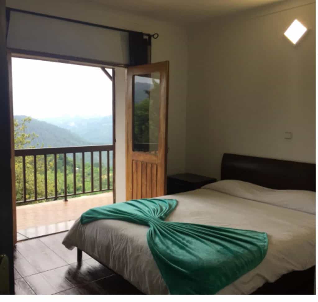 Bedroom with bed and balcony view of lush green mountains in Casa do Criado Gerês.