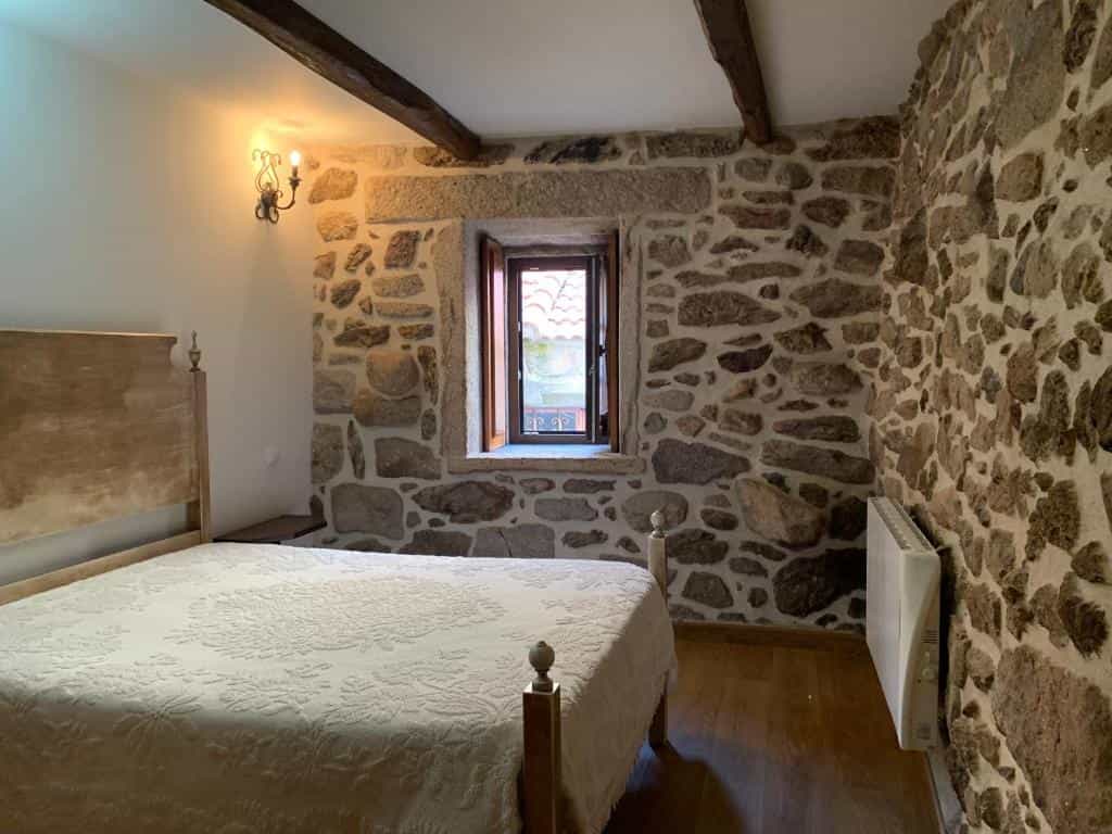 Bedroom with stone walls, wooden beams, and white quilted bedspread inside Casa D'Campo Ferreira