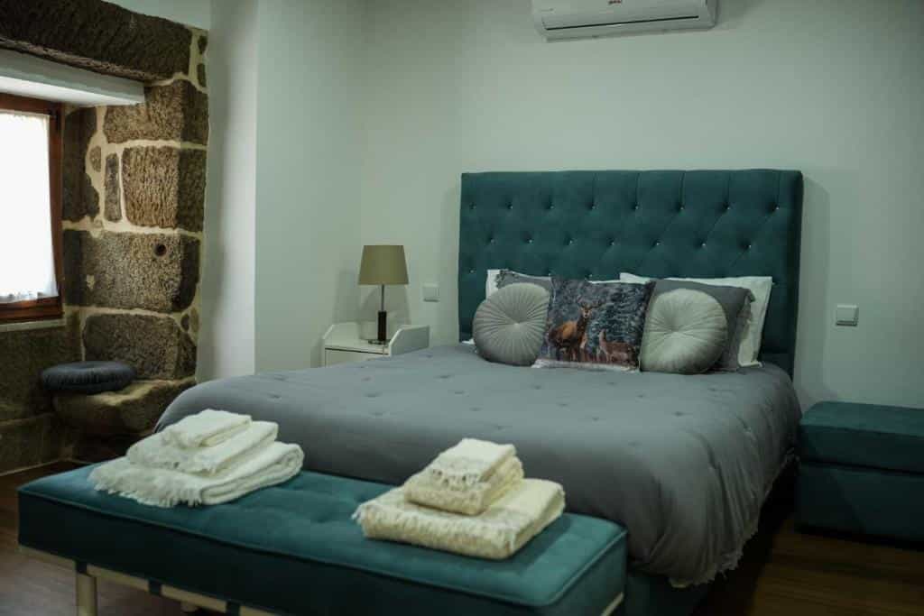 Bedroom with stone wall, teal tufted headboard, grey bedding, and folded white towels on a bench.