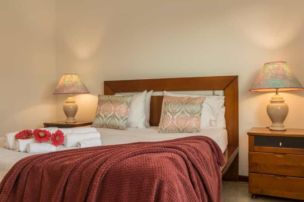 Bedroom with wooden bed frame, patterned pillows, red throw, and matching bedside lamps.
