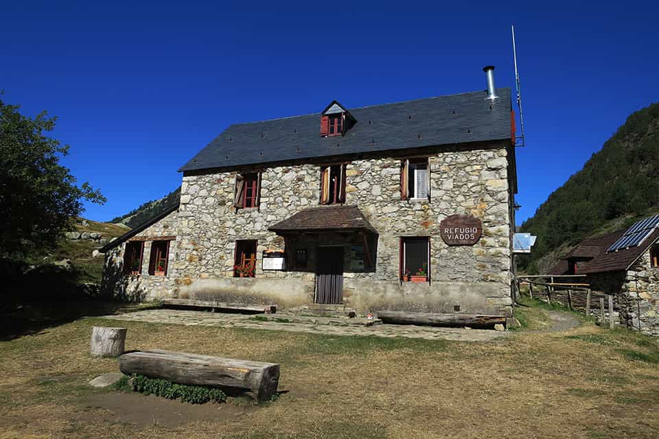 Refugio Viados stone mountain hut under clear blue sky with wooden benches.