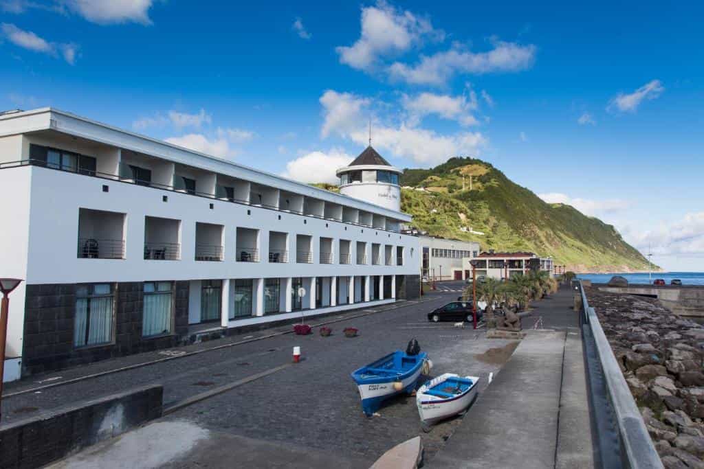White Hotel do Mar building by harbor with two small boats and green mountain backdrop.