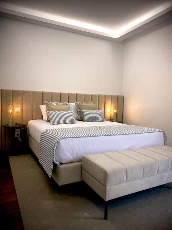 Modern hotel bedroom with beige upholstered headboard, striped throw, and lighted ceiling cove