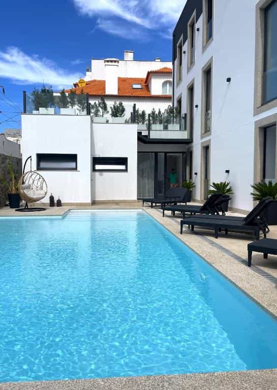 Outdoor swimming pool next to modern white hotel building with lounge chairs and hanging chair.
