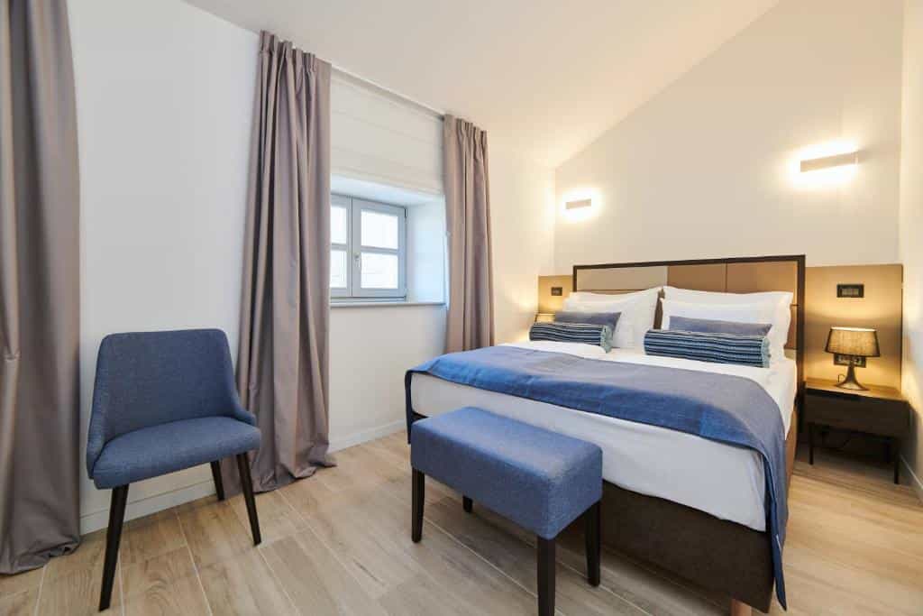 Bedroom with double bed, blue accents, and small window with gray curtains in Artegnana.