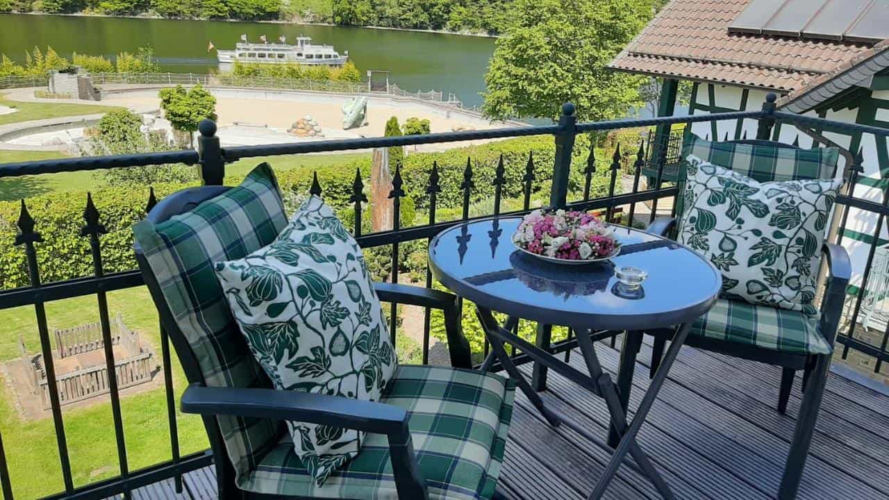 Balcony seating with lake view, boat on water, and green hillside in summer