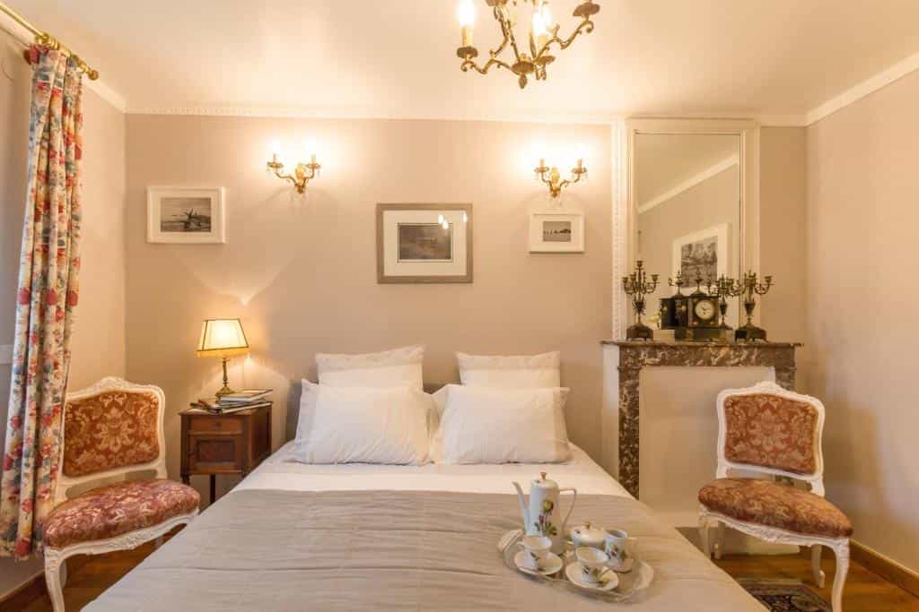 Bedroom with white bedding, antique chairs, fireplace, and tea service on bed