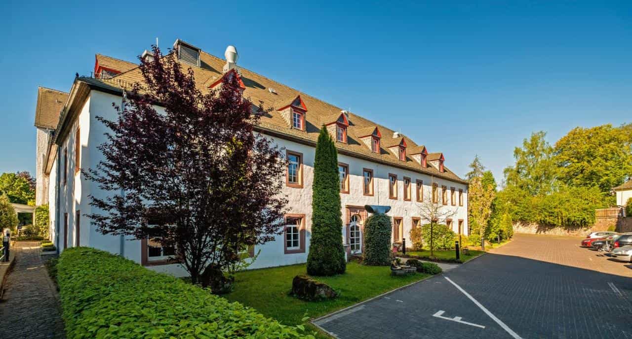 Augustiner Hotel building exterior with manicured lawn, trees, and paved parking lot.
