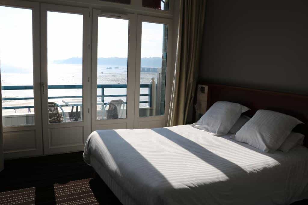 Bedroom with white striped duvet facing glass doors overlooking a low tide or shallow water view.