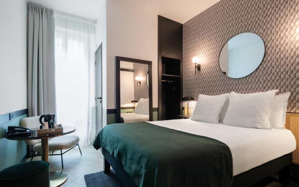Hotel room with double bed, patterned wallpaper, round mirror, and small seating area.