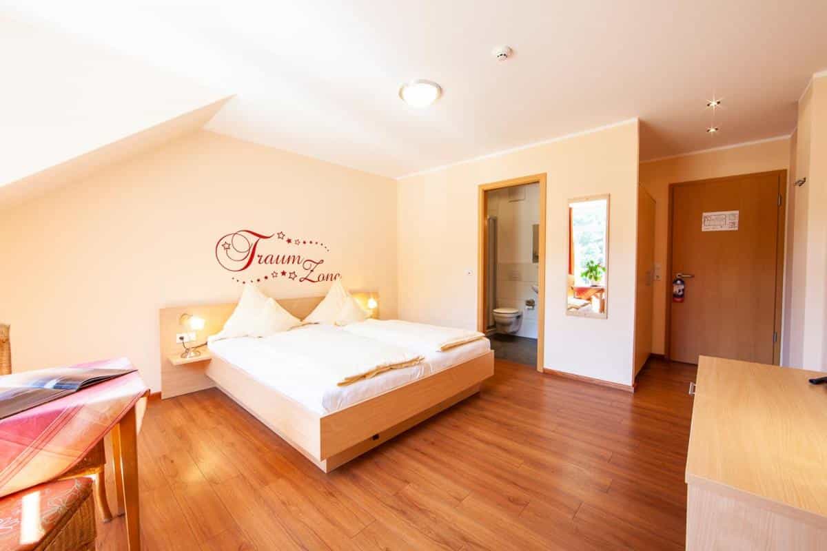 Hotel room with wooden floor, double bed, wall decal, and view into a bathroom.