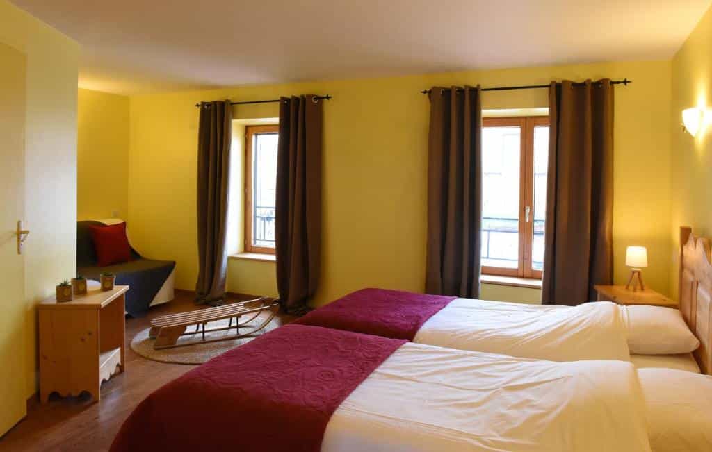 Twin beds with white and maroon bedding in a yellow room at Auberge du Couvige