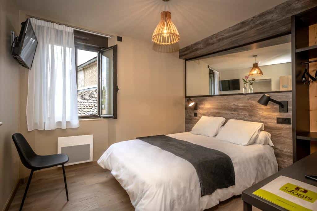 Logis hotel room with white bedding, wood accents, and open window view of rooftops