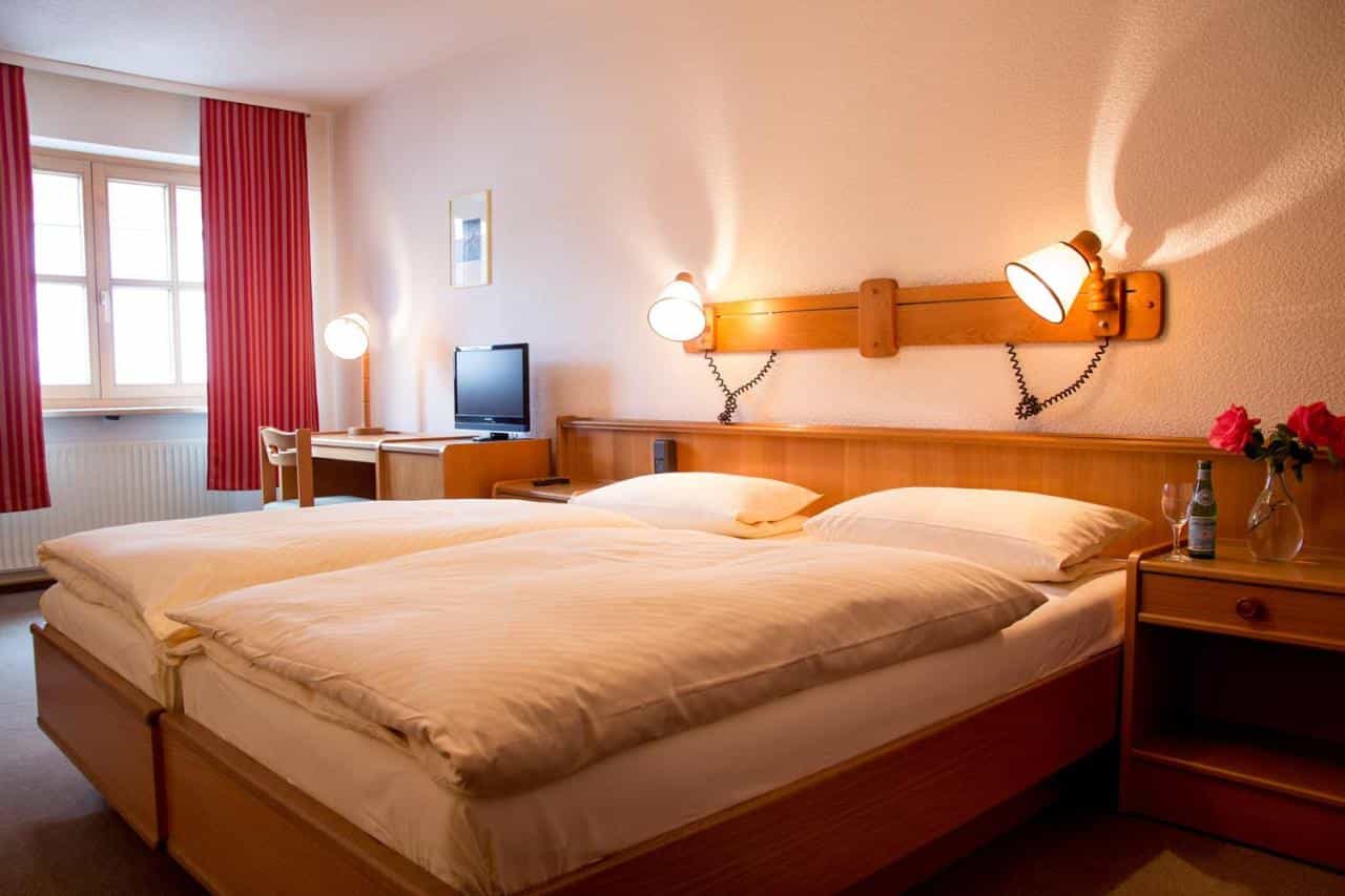 Twin beds with white linens in a hotel room with wooden furniture and red striped curtains.
