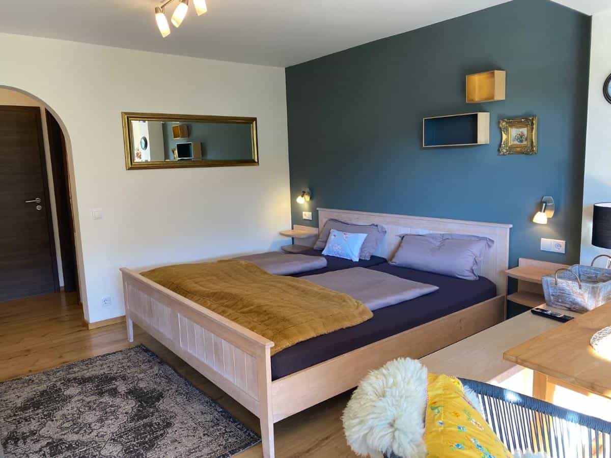 Bedroom with light wood bed, mustard throw, and dark teal accent wall in Ferienhaus Meixner.