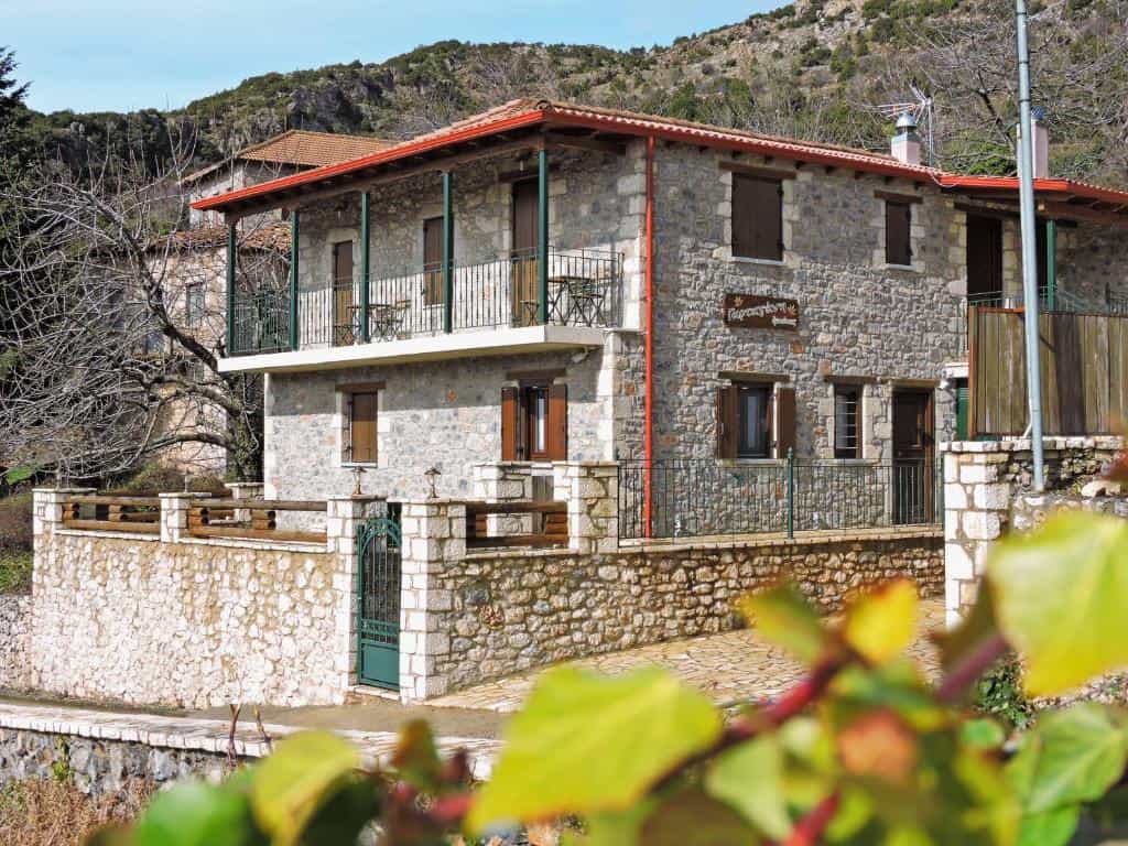 Stone guest house with balconies in a mountainous setting, foreground leaves blurred