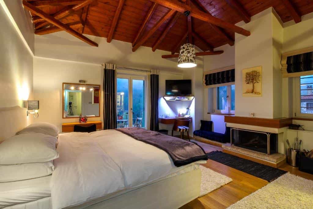 Bedroom with white bedding, wood beamed ceiling, fireplace, and balcony access at Enastron Guesthouse.