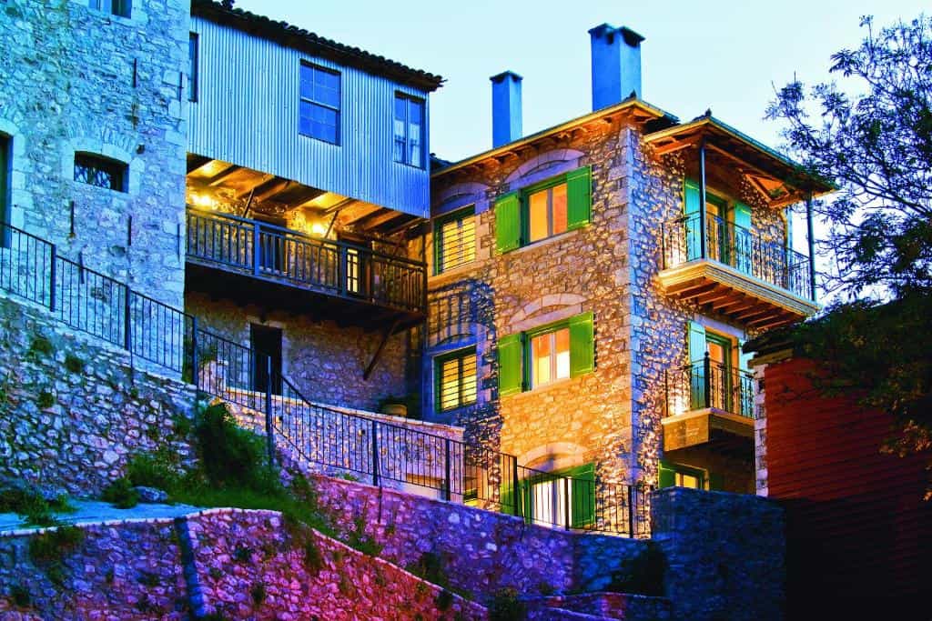 Stone guesthouse with illuminated windows and green shutters, built into a hillside at dusk