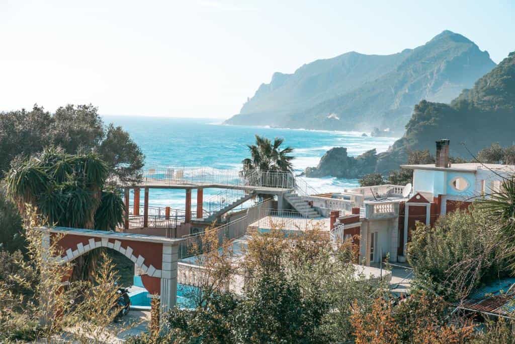 Coastal buildings with terraces overlooking turquoise sea and large green mountains.