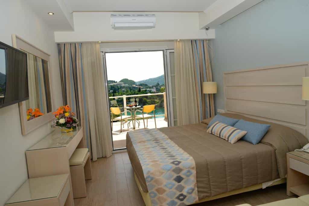 Hotel room with double bed, balcony view of green hills and coastal buildings