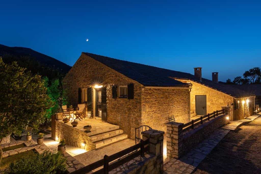 Illuminated stone merchant's house exterior at dusk with outdoor seating near mountains.