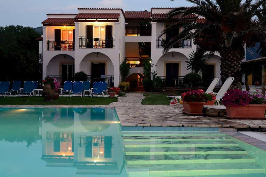 White apartment building with illuminated windows reflected in a swimming pool at dusk